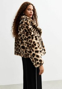 Giacca in pelliccia sintetica con stampa leopardata, colletto ampio, design corto e morbida consistenza. Presenta macchie nere e marroni su uno sfondo beige.