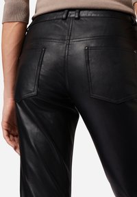 Zwarte leren broek met een gladde textuur, voorzien van minimalistische achterzakken en subtiele stikdetails langs de tailleband en naden.