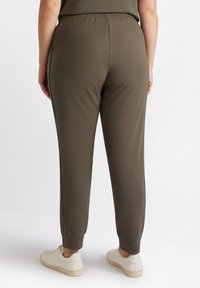 Olivgrön, stretchiga joggingsbyxor med elastiskt midjeband och avsmalnande anklar. Aningens med vita sneakers. Slät textur.