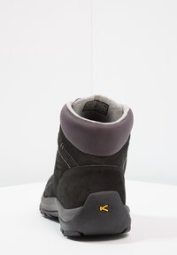 Botín de ante negro con un collar acolchado gris, superficie texturizada y un distintivo logo amarillo en el tacón.