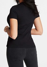 Camiseta de algodón negra con manga corta, diseño ajustado y un ligero dobladillo curvado. Combinada con jeans negros que tienen bolsillos traseros.