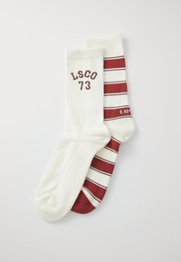 Two pairs of cotton socks. One is solid white with "LSCO 73" printed in brown. The other has red and white stripes with a logo in red.