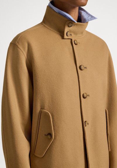 Καμηλό μαλλί παλτό με ψηλό γιακά, πέντε κουμπιά και δύο διαγώνιες τσέπες. Το ύφασμα έχει  απαλή υφή και καθαρό, δομημένο σχέδιο.