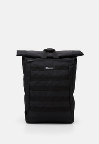 Sac à dos à rabat noir fabriqué à partir de tissu durable, avec une surface texturée, une poche zippée à l'avant et des sangles en sangle pour des accessoires modulaires.