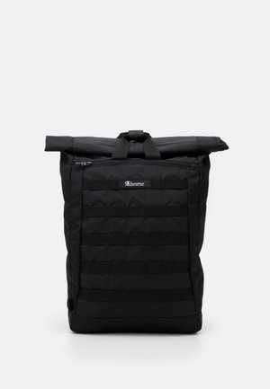 Sac à dos à rabat noir fabriqué à partir de tissu durable, avec une surface texturée, une poche zippée à l'avant et des sangles en sangle pour des accessoires modulaires.
