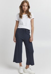 Navy ribbed wide-leg pants with drawstring waist; paired with a fitted white t-shirt and white sneakers, displaying a casual, relaxed style.