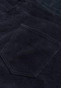 Tessuto in corduroy blu navy con strisce verticali, dotato di tasca patch. La texture è morbida, con righe ben definite e una finitura a cucitura pulita.