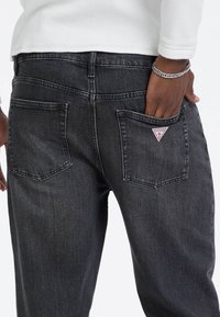 Ciemnoszare dżinsy o prostym kroju, z tylnymi kieszeniami i trójkątną metką w czerwono-białe wzory na prawej kieszeni.