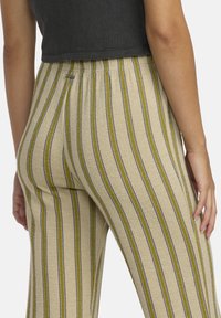 Pantaloni a maglia a righe in beige con strisce verticali verdi e blu. La vita elasticizzata e il tessuto testurizzato offrono comfort e flessibilità.