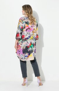 Färgglad blommig lång blus med trekvartslånga ärmar, tillverkad av lättviktsmaterial; kombinerat med mörka jeans och ljuslila klackar.