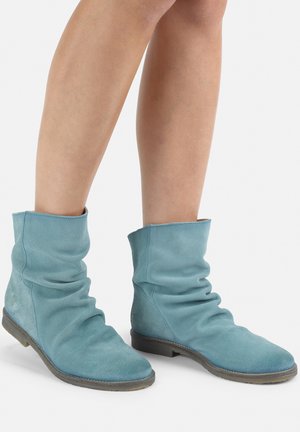 Stivaletti in suede blu con design arricciato, punta rotonda e suola piatta. La texture è morbida, caratterizzata da una silhouette casual e rilassata.