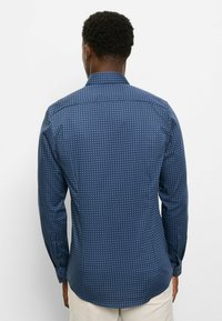 Dunkelblaues Langarmhemd mit weißem Punktmuster, ausgestattet mit einem klassischen Kragen, Knopfmanschetten und einem abgerundeten Saum. Glatter Baumwollstoff.