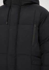 Chaqueta acolchada negra con un diseño con acolchado, capucha y dos bolsillos con cremallera. Fabricada con un material suave y duradero con un acabado mate.