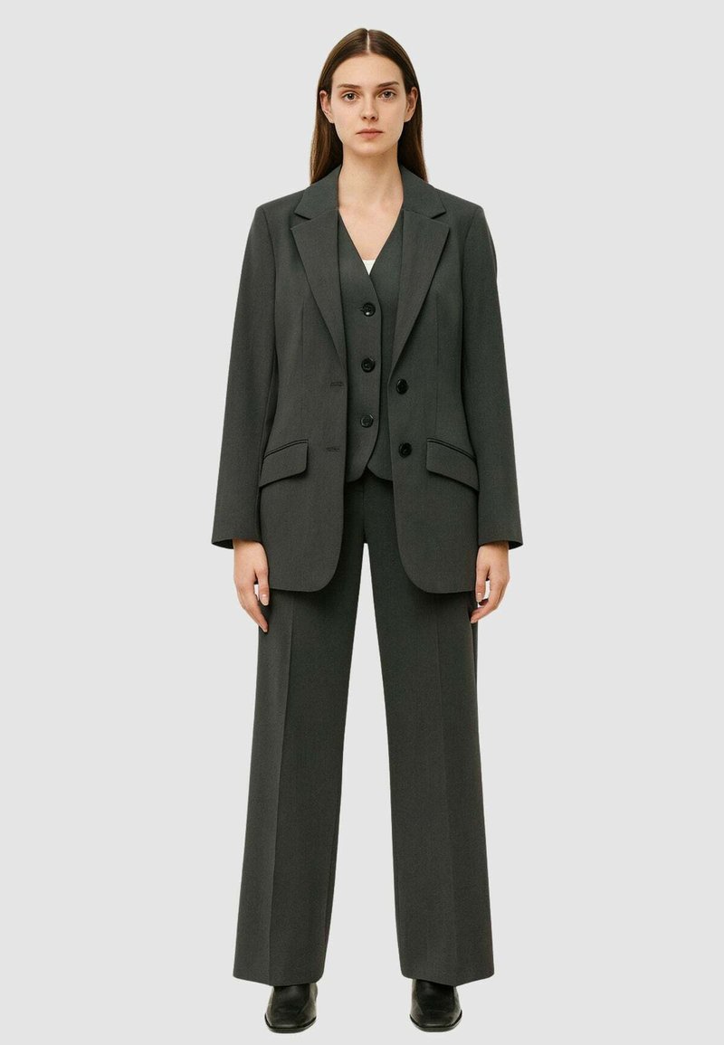 Completo grigio a tre pezzi composto da un lungo giacca, un gilet aderente con bottoni e pantaloni a gamba larga. Tessuto liscio con un design strutturato.