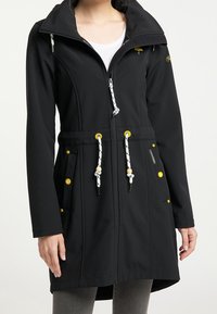 Black waterproof jacket with a high collar, textured fabric, yellow accents, elastic drawstrings, and side pockets with button closure.