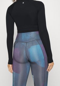 Top nero a maniche lunghe con design aderente abbinato a leggings a vita alta con motivo astratto multicolore in blu e viola.
