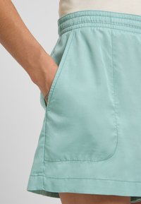 Hellblauer Rock mit einem elastischen Taillenbund und Seitentaschen, der eine glatte Textur und einfache Stichdetails aufweist.