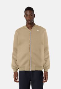Giacca bomber khaki con zip frontale, polsini e orlo a costine, dotata di un piccolo logo sul petto e dettagli con zip a strisce multicolori.