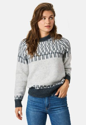 Gray and white patterned sweater with a dark knit collar and cuffs, featuring abstract designs and a relaxed fit, paired with blue jeans.
