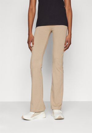 Pantaloni beige a palazzo realizzati in tessuto elastico, con una texture liscia, abbinati a scarpe da ginnastica bianche. Design semplice senza motivi visibili.
