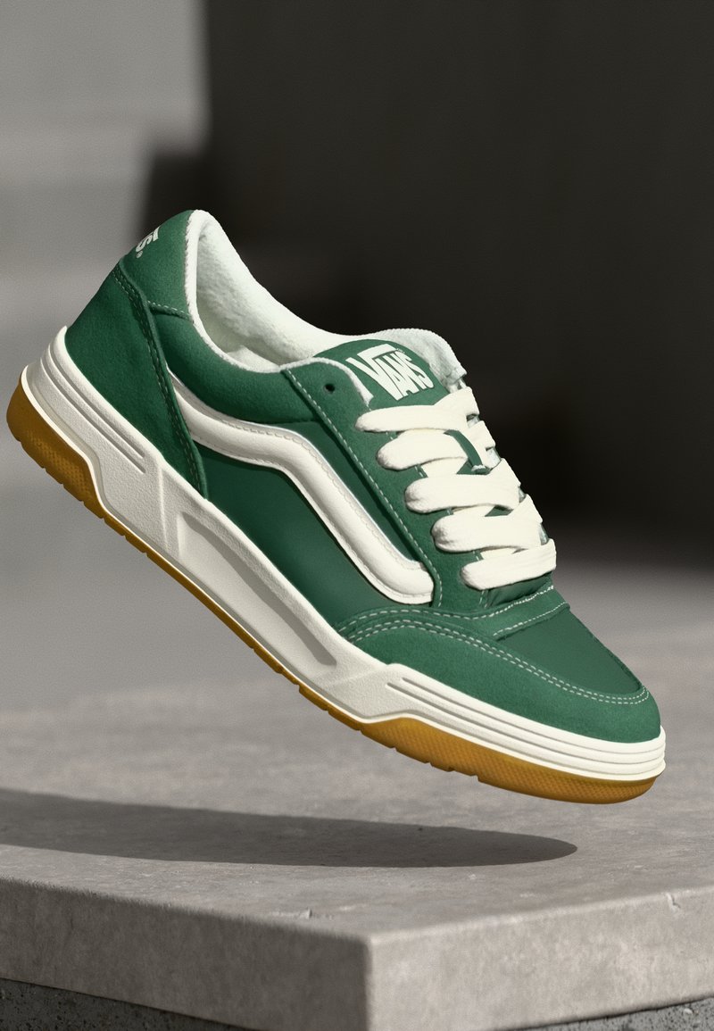 Gröna lädersneakers med vita accenter, vadderad krage, tjocka snören och en texturerad gummisula. Klassisk låg modell.