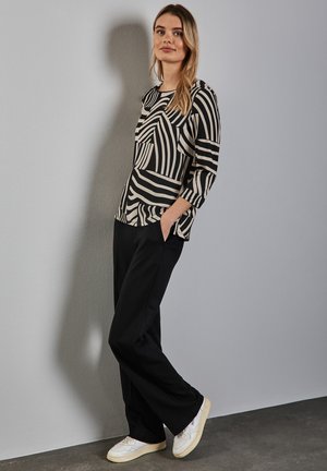Blusa a righe bianco e nere con maniche a tre quarti, abbinata a pantaloni neri e sneakers bianche. Tessuto morbido, vestibilità comoda, tasche laterali.