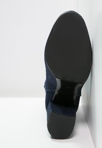 Chaussure à talon haut bleu marine avec un tissu supérieur texturé, semelle noire lisse et un bout légèrement pointu. Taille 37 visible sur la semelle.