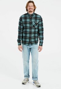 Geruite flanellen overhemd in turquoise en zwart, met een button-up voorkant, kraag en borstzak; gedragen met lichte spijkerbroek en sneakers.