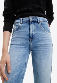 Ljusblå denimjeans med slim fit, lätt slitning, fem fickor och mid-rise midja med metallknappslutning.