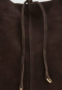 Bolso de ante marrón con cierre de cordón, que presenta dos ojales de metal en tono dorado y costuras en contraste a lo largo de los bordes.