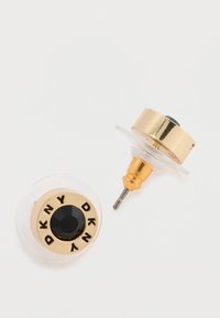 Boucles d'oreilles dorées avec un centre en pierre noire, arborant "DKNY" gravé autour du bord. Arrière transparent, design rond et texture polie.