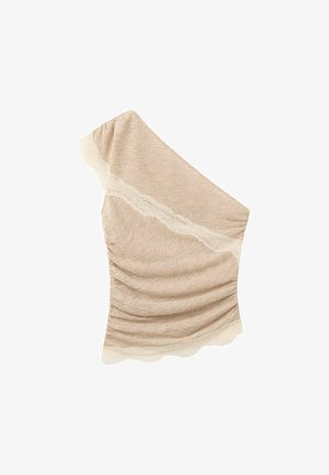 Haut beige à une épaule avec tissu froncé et délicate bordure en dentelle le long de l'encolure et de l'ourlet sur fond blanc.
