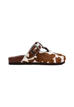Zapatos slip-on de piel de vaca con un patrón marrón y blanco, que cuentan con una hebilla ajustable de plata y una suela marrón. Acabado en piel texturizada.