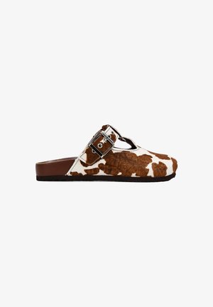 Zapatos slip-on de piel de vaca con un patrón marrón y blanco, que cuentan con una hebilla ajustable de plata y una suela marrón. Acabado en piel texturizada.