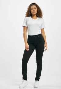 Svarte høytaljede jeans med slim fit, kombinert med en tettsittende hvit t-skjorte. Brukt med hvite sneakers og store hoop-øreringer.