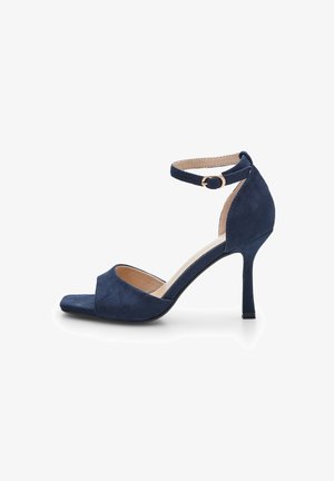 Tamno plave suede štikle s otvorenim prstima, pojasom oko gležnja i teksturiranom završnom obradom. Imaju elegantan dizajn tankog potplata.