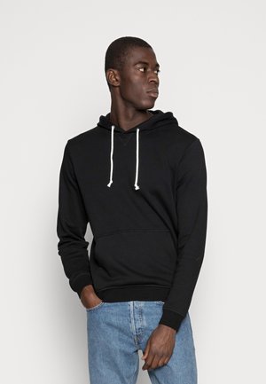 Haut à capuche noir avec une poche avant, un cordon de serrage pour la capuche et des poignets côtelés. Porté avec un jean bleu clair, au toucher lisse et à la coupe décontractée.