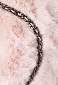 Metalowy łańcuch z grubymi ogniwami spoczywający na miękkiej, puszystej różowej tkaninie; łańcuch ma błyszczące wykończenie i naprzemienne płaskie oraz zakrzywione kształty ogniw.
