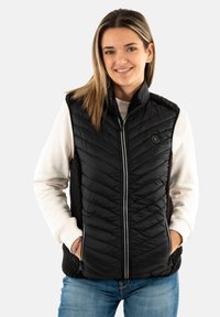 Gilet nero trapuntato con colletto alto e chiusura a zip. Tasche laterali e tessuto texturizzato sui lati. Indossato sopra un maglione leggero.