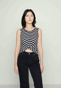 Povezan črno-beli črtast top brez rokavov s krožnim izrezom in krajšim krojem, v kombinaciji z visokim pasom črnimi kavbojkami.