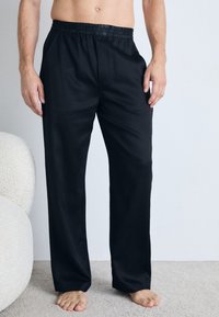 Black, loose-fitting pants with an elastic waistband, made from a smooth fabric, featuring side pockets and a straight-leg design.