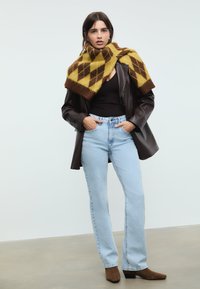 Smeđi kožni blejzer, crni top na bretele, svijetloplave traperice ravnog kroja i žuto-smeđi karirani šal prebačen preko ramena, uz smeđe čizme do ankle.