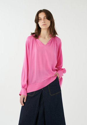 Blusa leggera rosa con scollatura a V e vestibilità rilassata, dotata di maniche lunghe con polsini arricciati. Abbinata a una gonna di jeans scura.