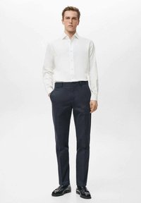 Camisa blanca abotonada, pantalones oscuros a medida, tela suave, corte ajustado, diseño minimalista y zapatos de cuero negro pulido.