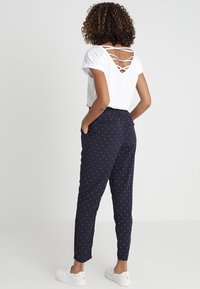 Vit kortärmad topp med korsad ryggdesign, tillsammans med marinblå byxor med vita prickar, elastisk midja och sidofickor.