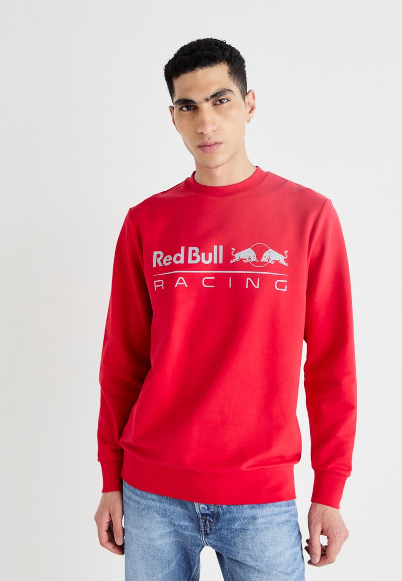 Sudadera roja con cuello redondo, que presenta el logo "Red Bull Racing" en blanco. El material es suave; los puños y el dobladillo son acanalados.