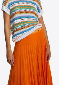 Monivärinen neulottu lyhythihainen paita, jossa on oranssin, sinisen ja valkoisen raidoitus. Pitkä, laskostettu oranssi hame, jossa on istuva vyötärönauha.