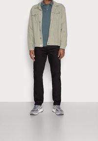 Ljust grå denimjacka, teal polotröja, svarta byxor och grå sneakers. Jackan har framfickor och knappdetalj.