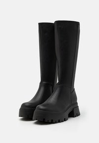 Black knee-high boots made of smooth synthetic material. Features a chunky sole with deep tread, side zip closure, and rounded toe design.