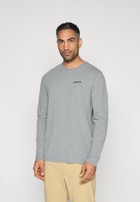 Γκρι μακρυμάνικο μπλουζάκι από μαλακό ύφασμα, με στρογγυλή λαιμόκοψη και μικρό μαύρο λογότυπο "Patagonia" στο πάνω αριστερό μέρος του στήθους.